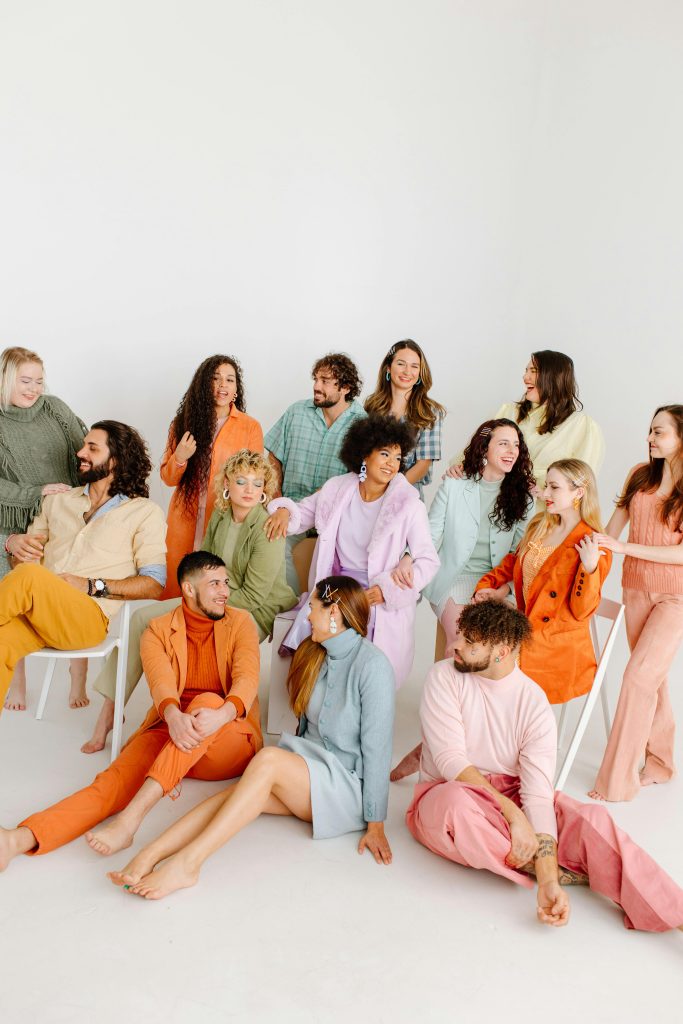 Diverse group of adults in vibrant pastel clothing posing happily in a studio.