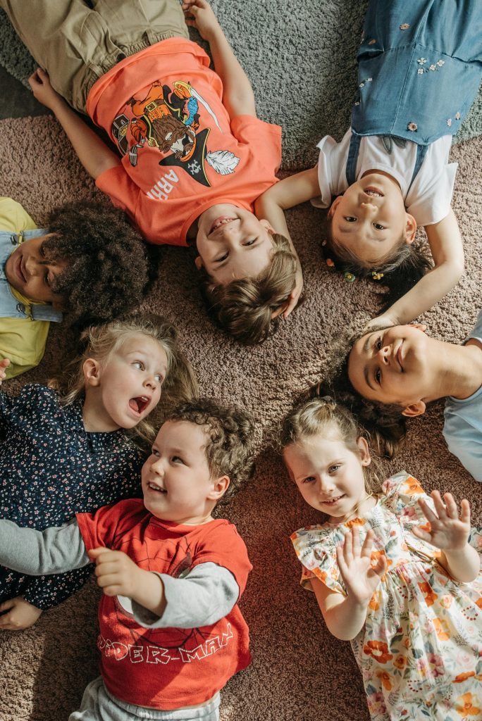 Joyful group of diverse children lying in a circle on a carpet, smiling and having fun.